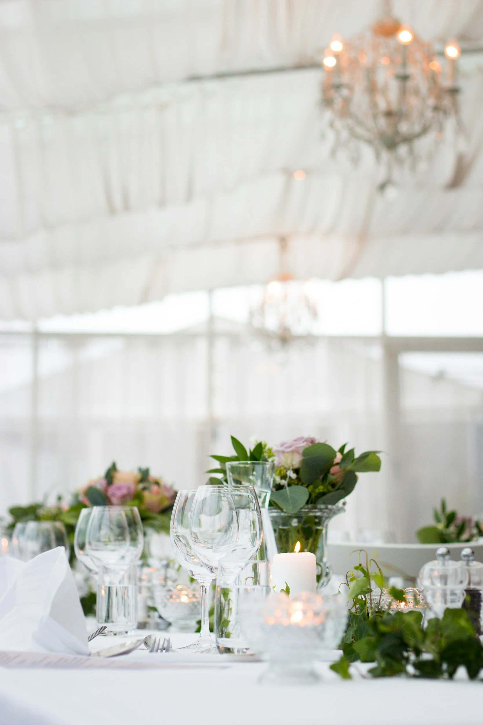 jksrentals A decorated dinner table with glassware, candles, and floral arrangements in a bright, elegant setting with hanging chandeliers.