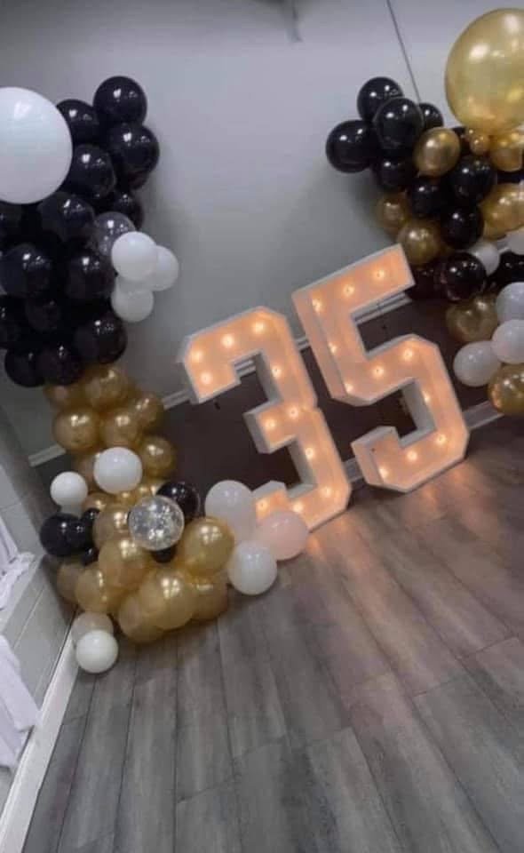 Celebration decor with a large illuminated number 35, and balloons in black, white, gold, and transparent colors arranged around the number.