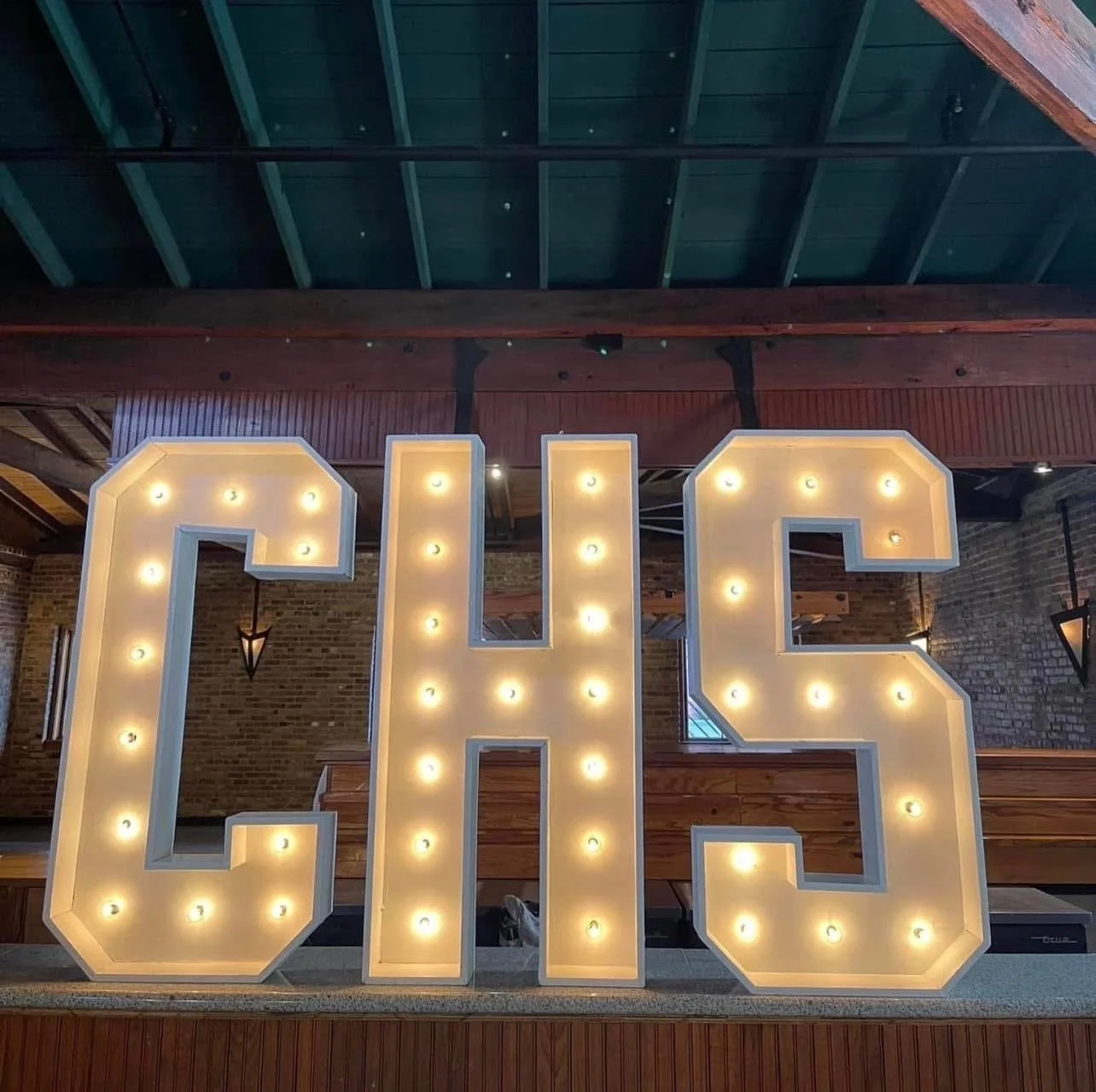 Decorative sign with the word 'LOVE' in large illuminated letters with light bulbs, placed against a brick wall inside a rustic-style building.