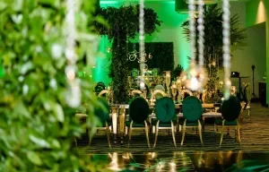 Elegant banquet table set in a lavish green and gold-themed room with lush greenery and ornate decorations.