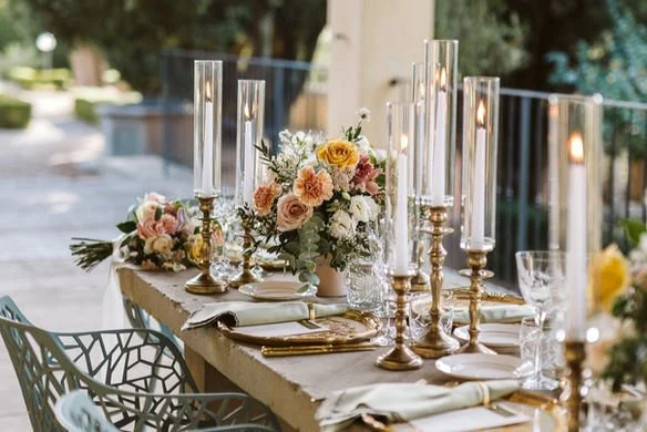 Elegant outdoor table setting with floral centerpieces, tall candles, and glassware