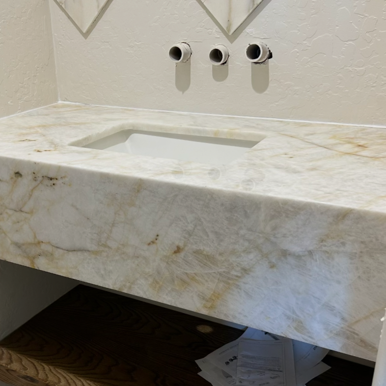 Bathroom vanity with a marble countertop and an empty sink, with three wall-mounted plumbing pipes above, and some papers underneath.