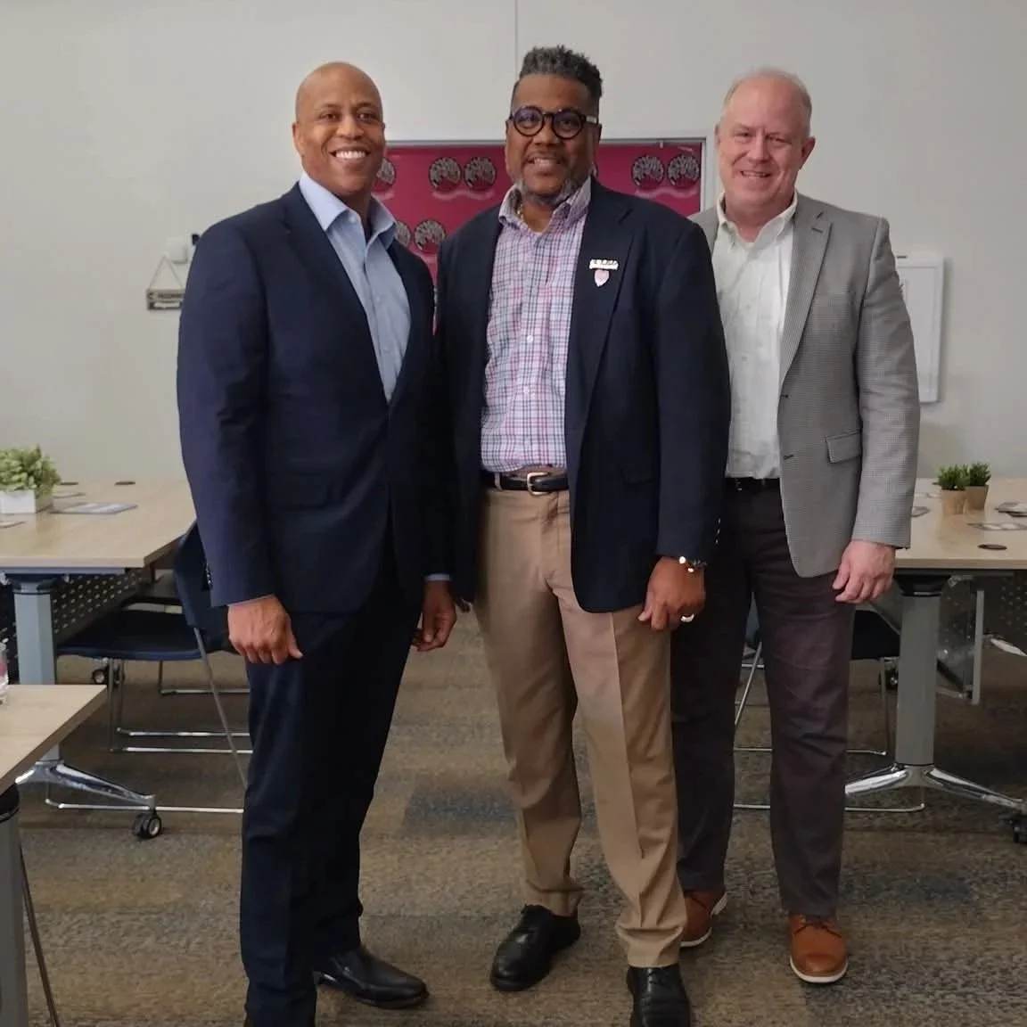 Three men dressed in formal attire standing together in a conference room, smiling for the camera.