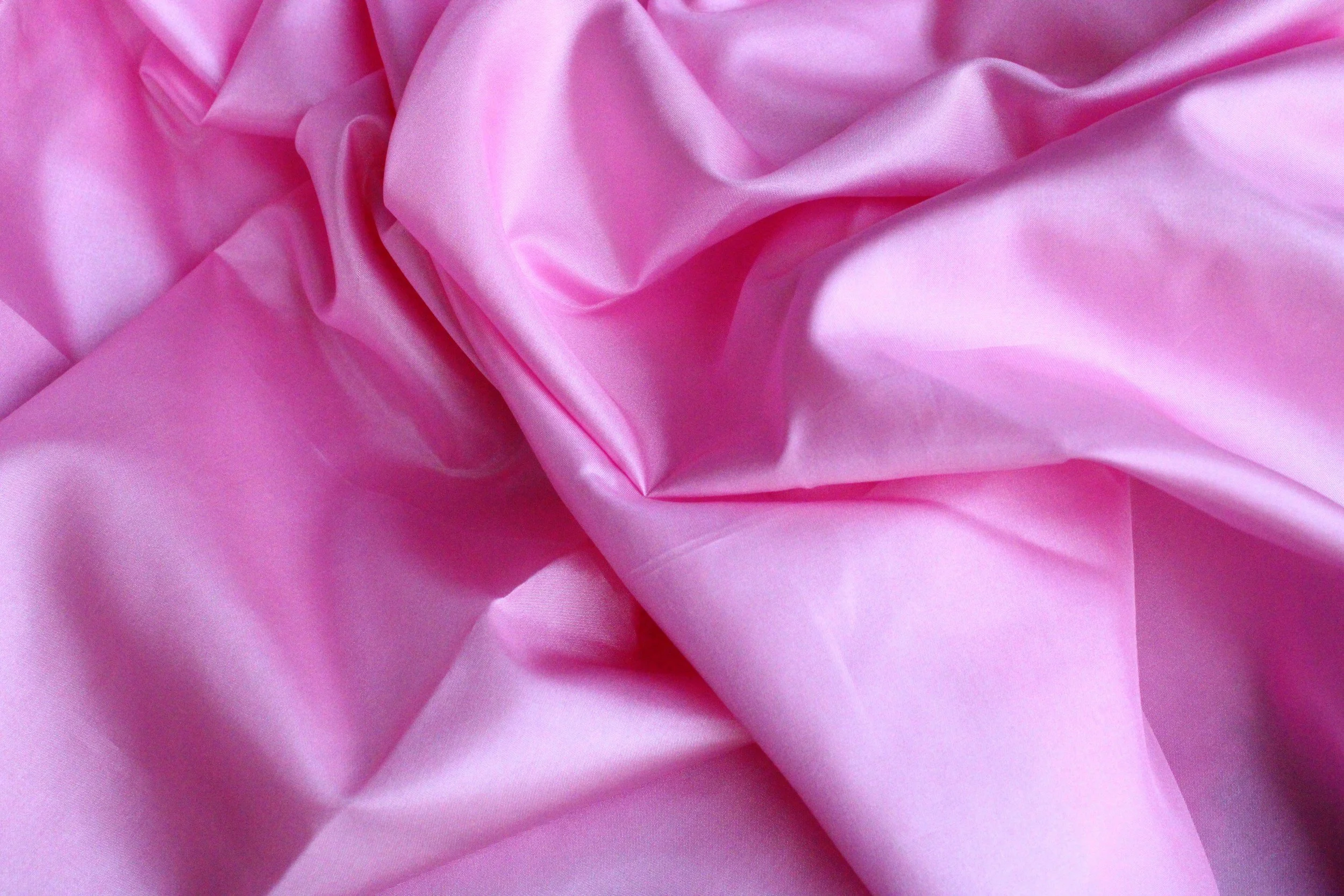 Close-up of pink, silky, ruffled fabric with folds and smooth texture.