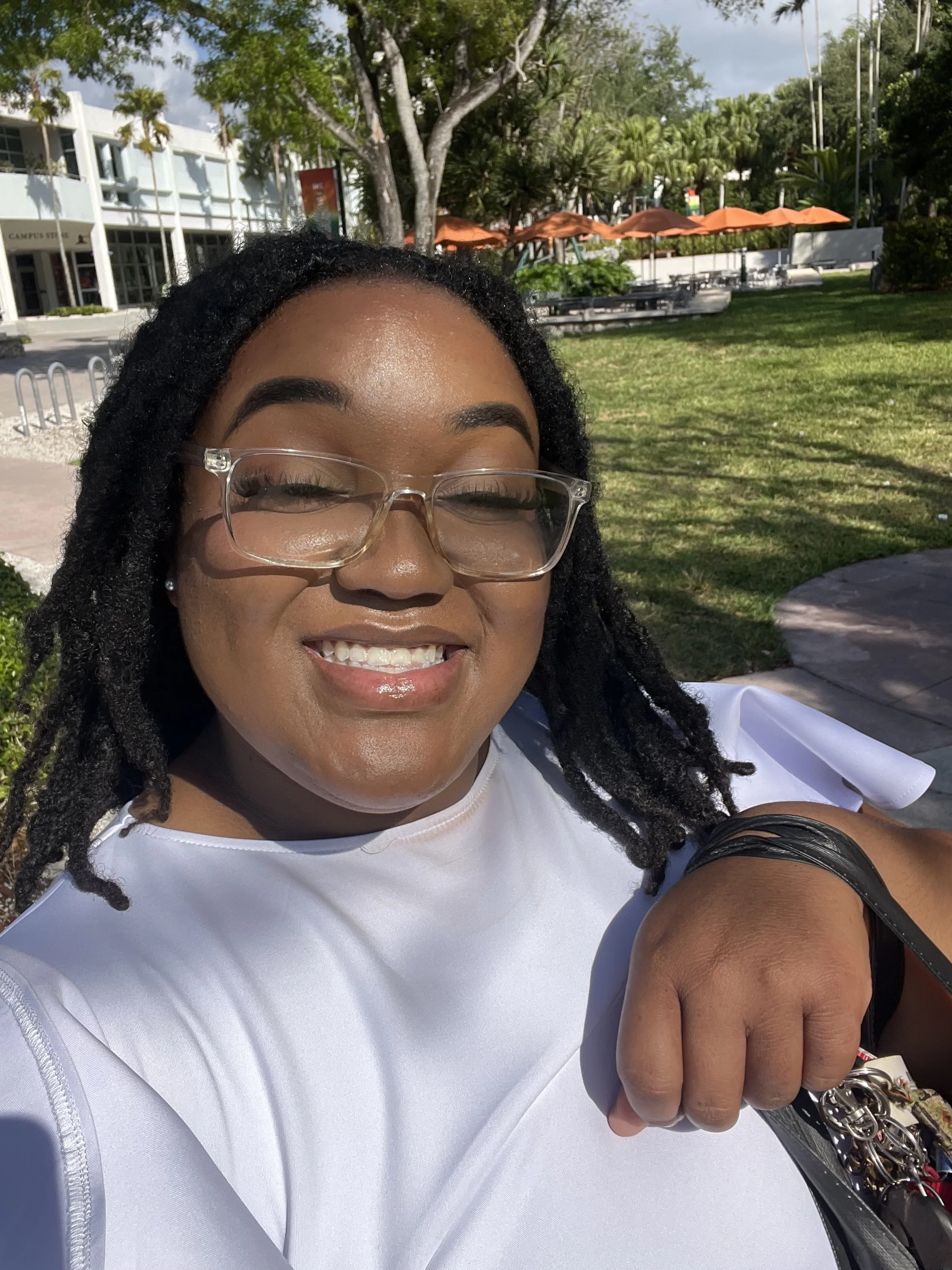 Zanaiah Billups smiling in a white dress and glasses at a campus