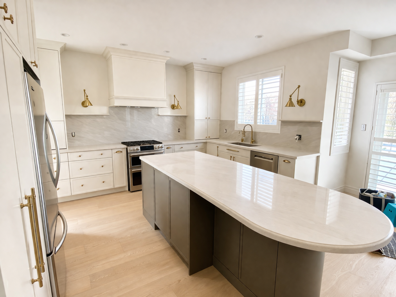 Modern kitchen with white cabinets, gold hardware, a kitchen island with a marble countertop, stainless steel appliances, and large windows with white plantation shutters.