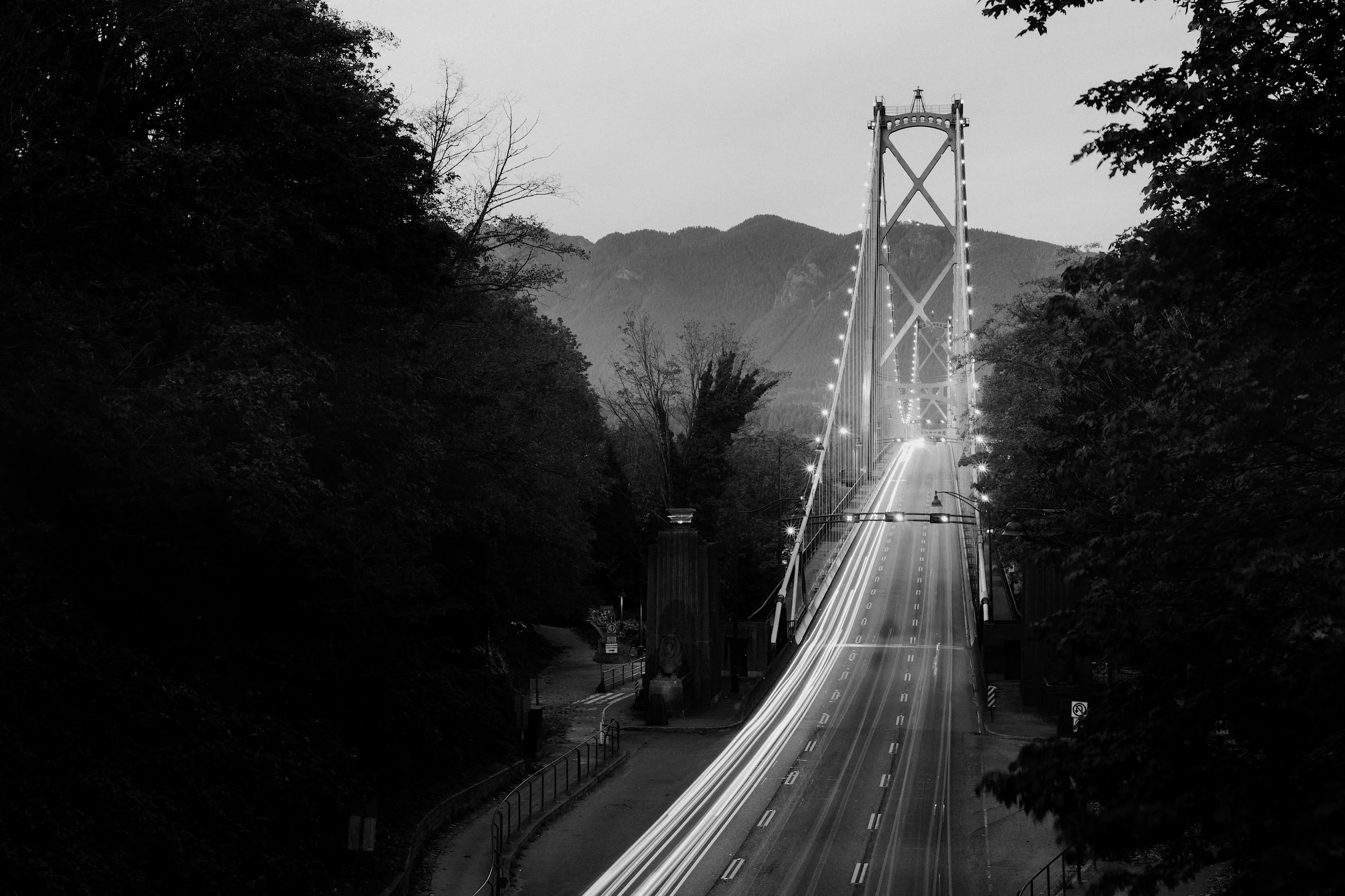 Vancouver Canada black and white photo of a bridge, viewed through trees and towards the north Vancouver mountains.