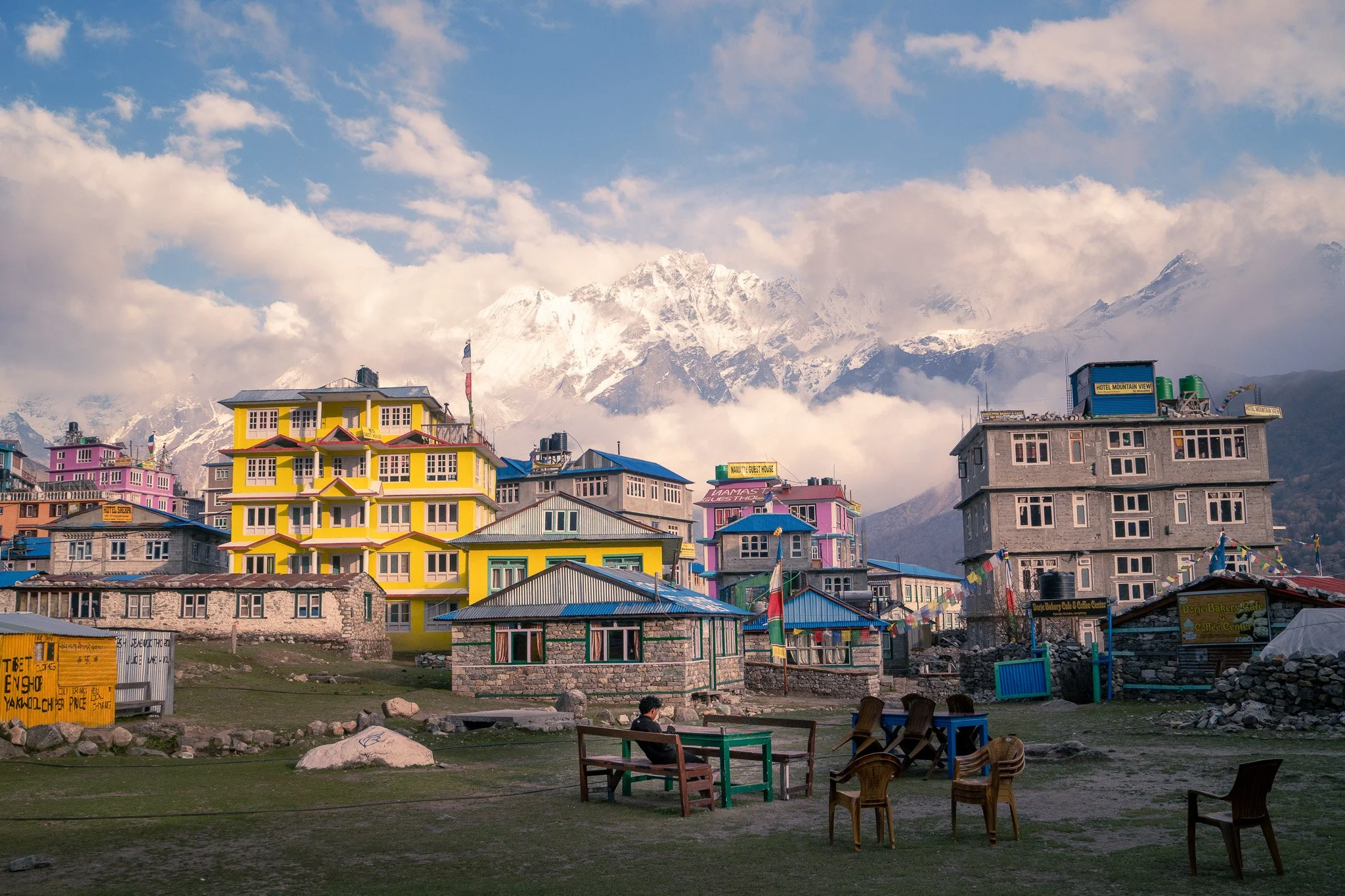 Colorful buildings on a hillside with mountainous background, a person sitting at a table in the foreground.