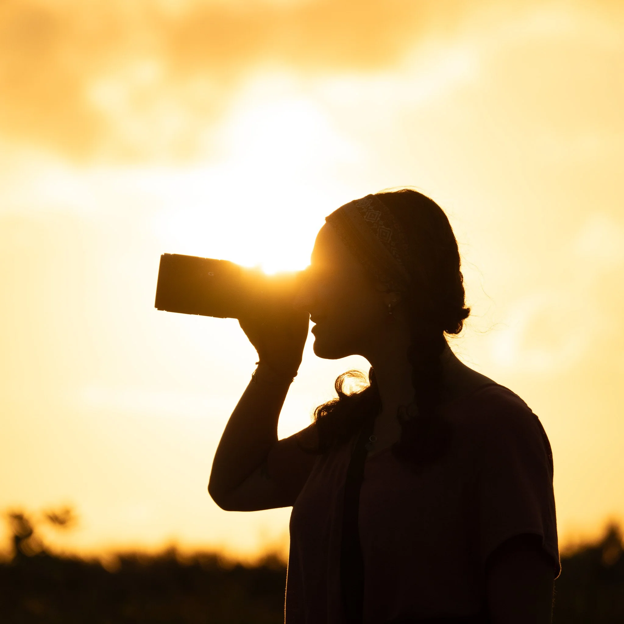Silhouette of a woman looking through a telescope at sunset.