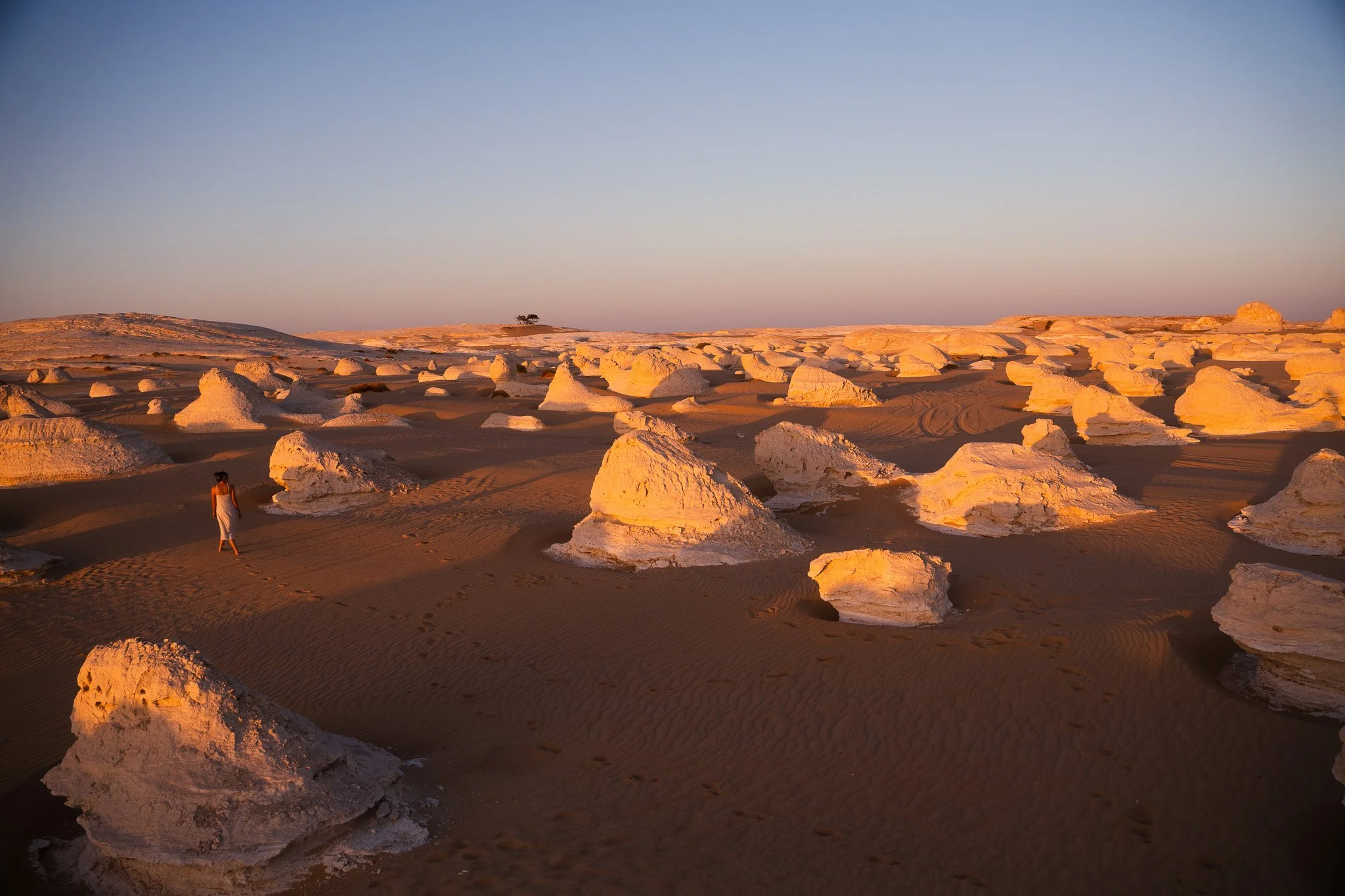 A person walking in a desert landscape with scattered white rock formations under a clear sky at sunset.