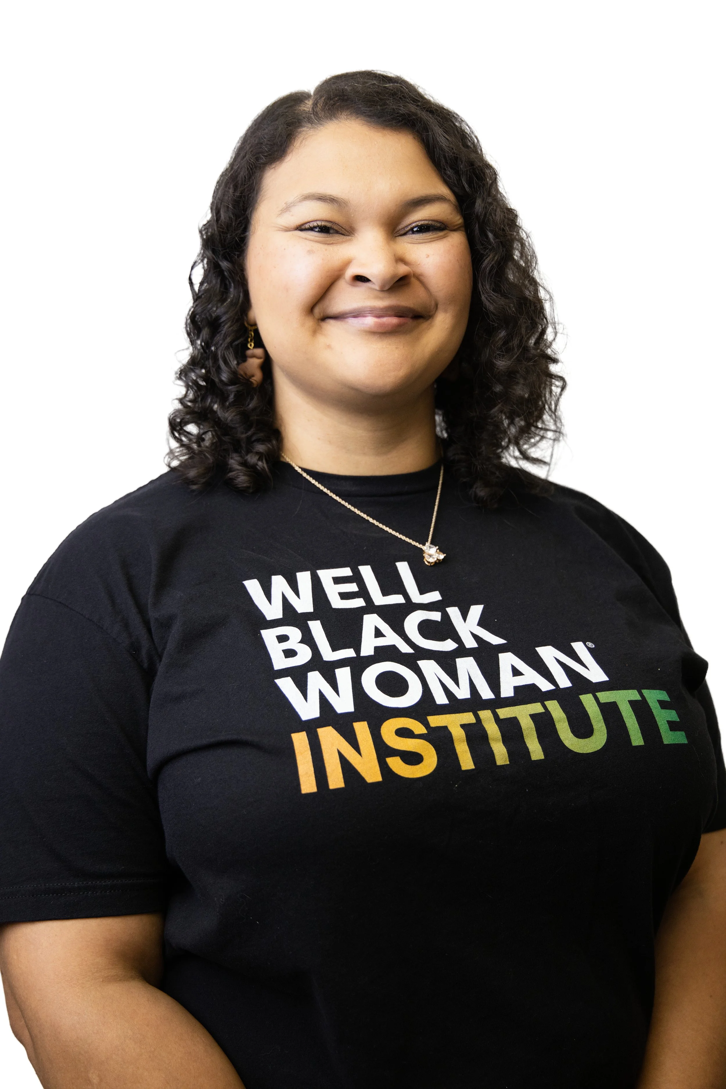 A woman with curly dark hair smiling, wearing a black T-shirt with colorful text that says "Well Black Woman Institute" and gold jewelry.