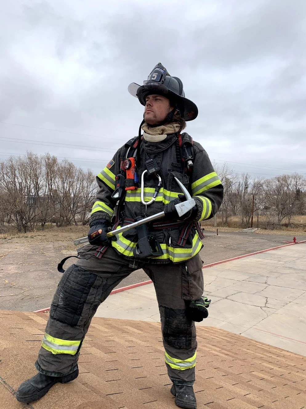 Firefighter in full gear holding a halligan tool outdoors on a cloudy day.