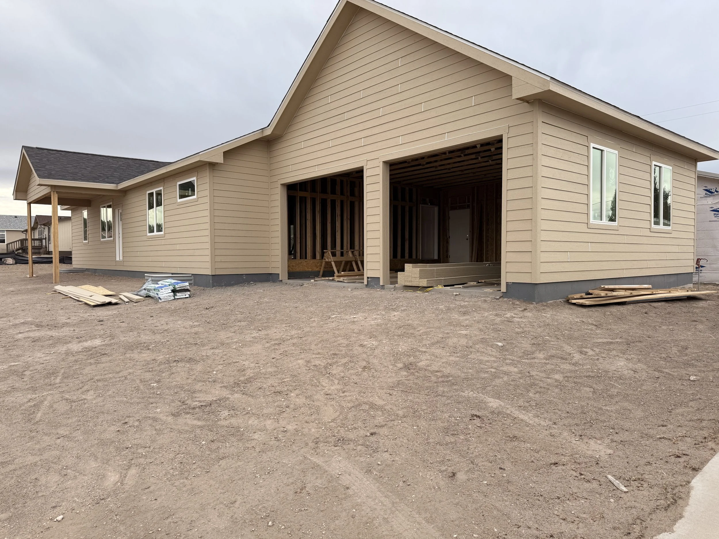 New beige-colored house under construction with some outer walls and windows installed, but unfinished garage area and no landscaping yet.