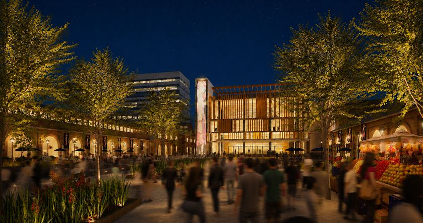 Night view of an outdoor public space with trees, market stalls, and a modern building with glass windows and vertical wooden slats, with people walking and shopping.