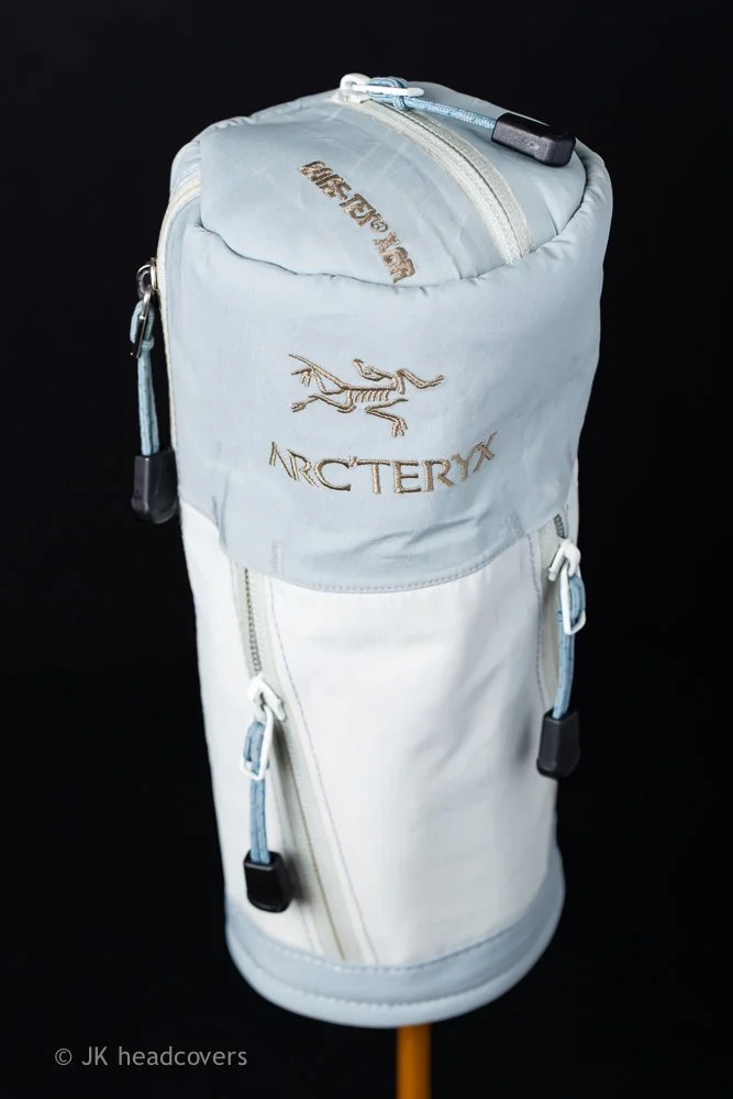 White Arc'teryx golf bag with multiple zippered compartments and zipper pulls, against a black background.