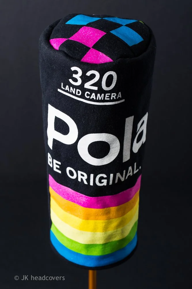 A rolled-up black sock with colorful rainbow stripes and the text 'POLE BE ORIGINAL' and '320 LAND CAMERA' on it. The top of the sock has a diamond pattern in pink, blue, and black.
