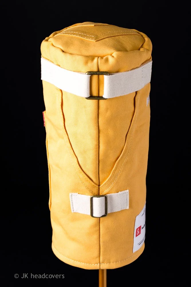 Yellow mannequin headcover with white straps, designed for golf club protection, against a black background.