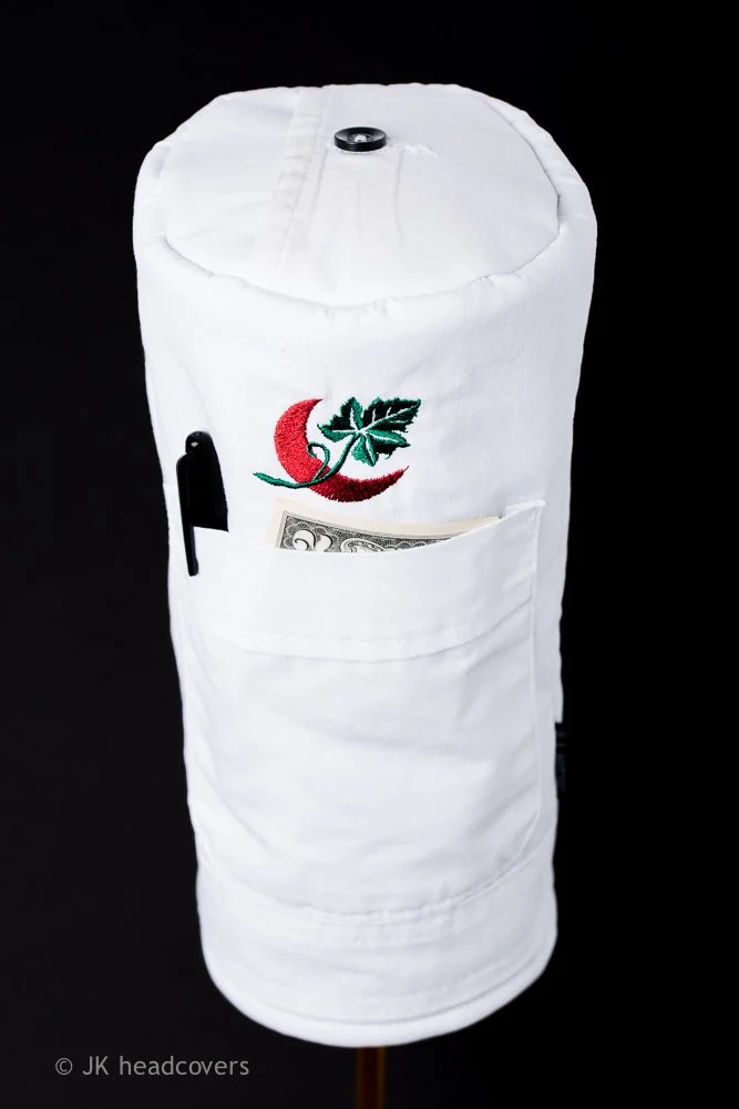 White fabric roll with embroidered chili pepper and leaf design, a pen in the pocket, and cash inside the pocket, set against a black background.