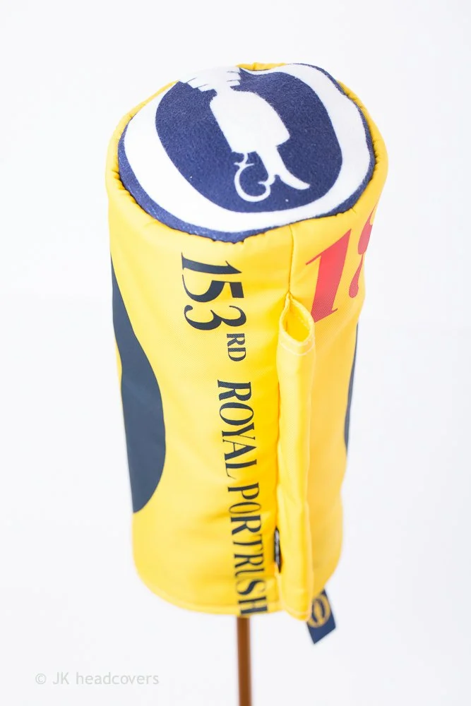 Golf-themed decorative item resembling a golf hole with a flag, featuring bright yellow and navy colors, displaying the number 153 and text about Royal Port Goth. It appears to be a souvenir or decorative piece.