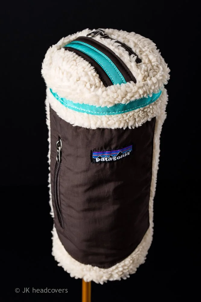 A Patagonia insulated water bottle holder with a fleece lining, black zipper, and logo, mounted on a yellow stick against a black background.
