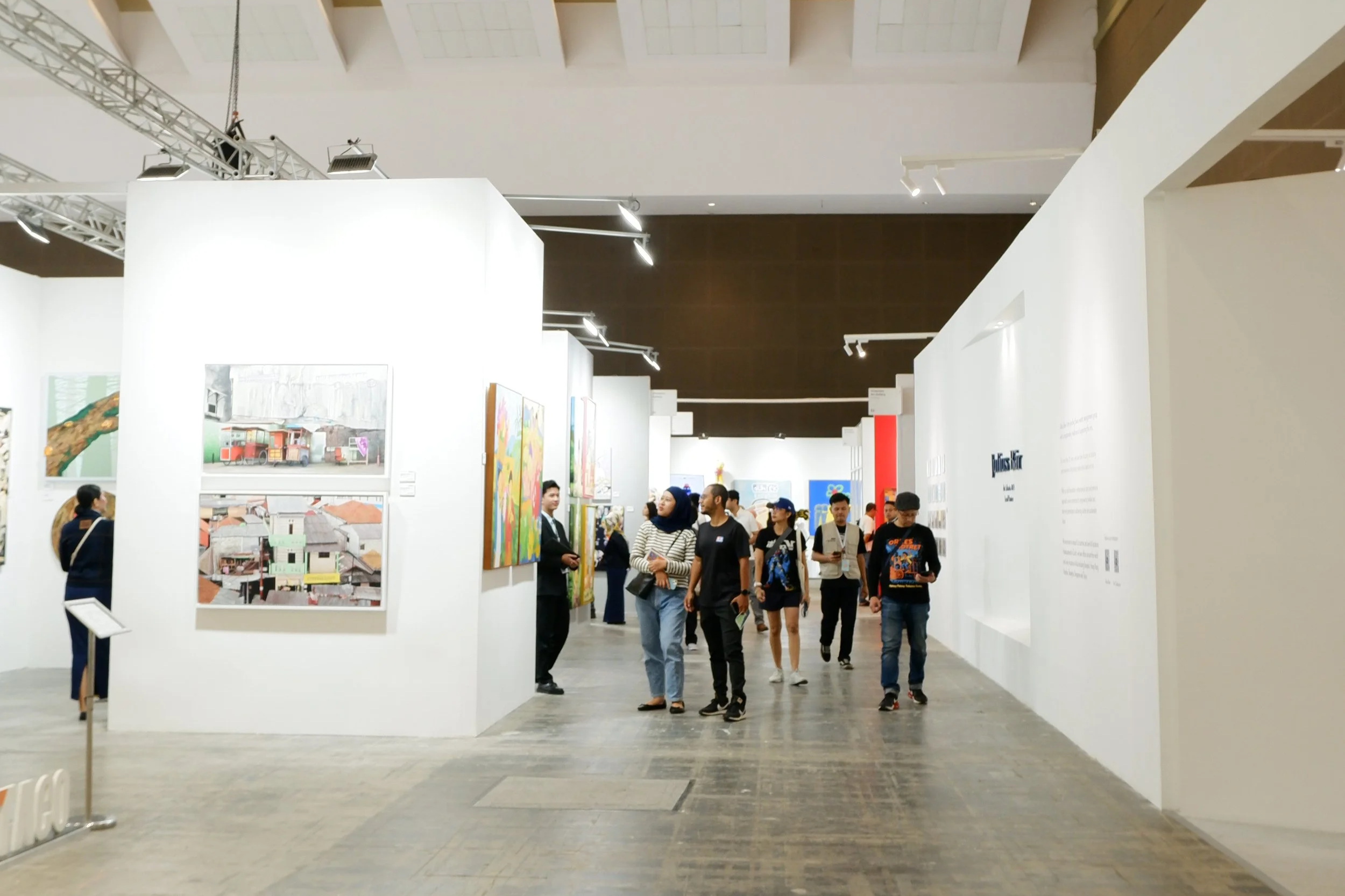 People walking through an art gallery with various artworks displayed on white walls.