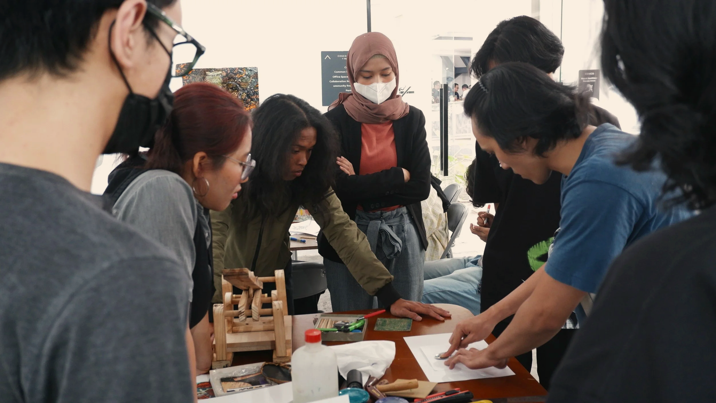 A diverse group of people gathered around a table, intensely focused on a hands-on craft or project, with various tools and materials on the table.
