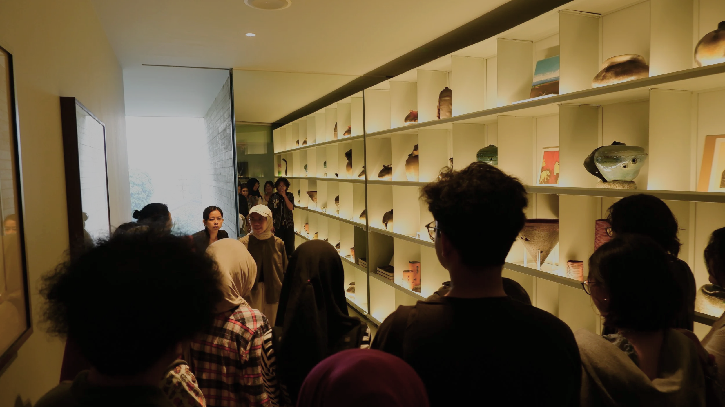 People gathered inside a museum room observing displayed artifacts on shelves with illuminated backgrounds.