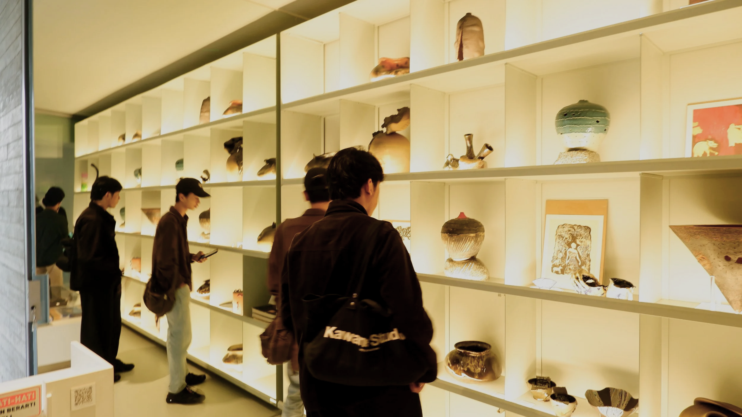 People looking at ceramic art pieces on illuminated shelves in an art gallery.