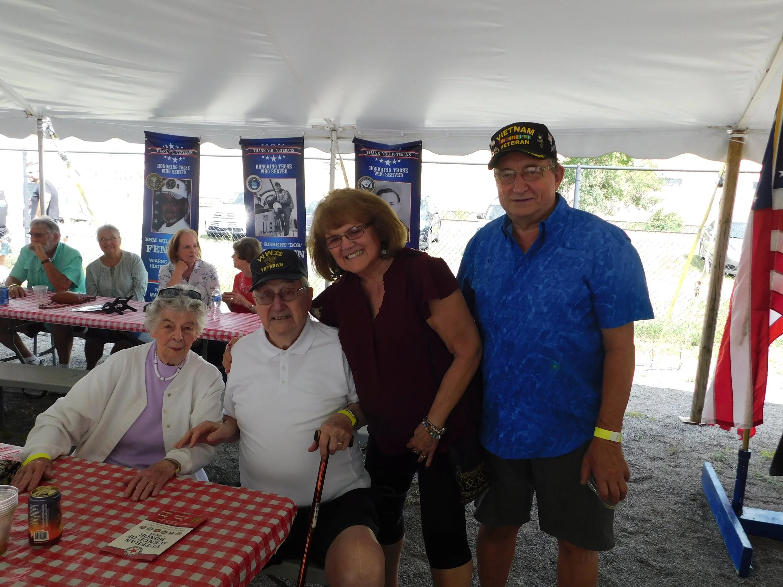 Group of people gathered under a tent at a Veteran's event, with some wearing caps that say 'Vietnam Veteran.'