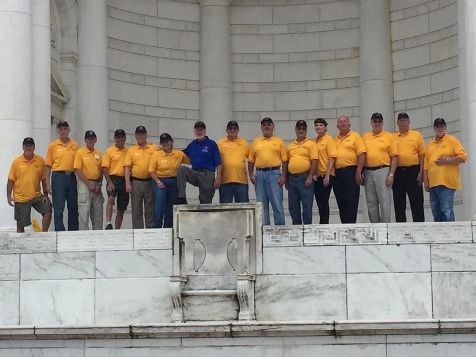 A group of people wearing yellow shirts and caps standing on a marble structure in front of the Lincoln Memorial.