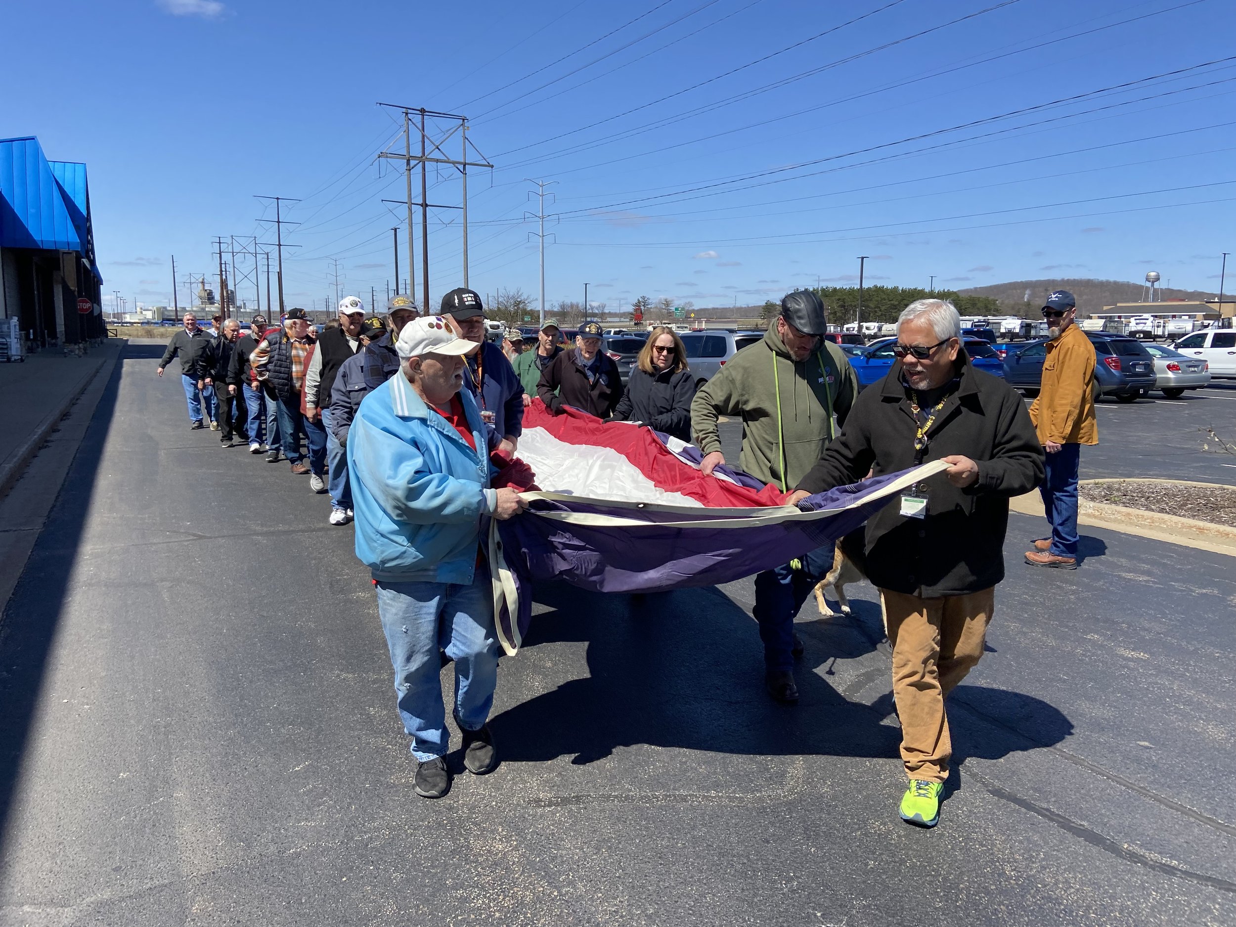 A group of people walking outdoors in a line, holding a large flag or banner.