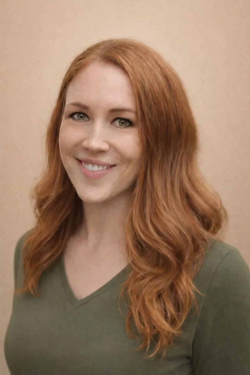 Portrait of a woman with long, wavy red hair, wearing an olive green shirt, smiling against a beige background.