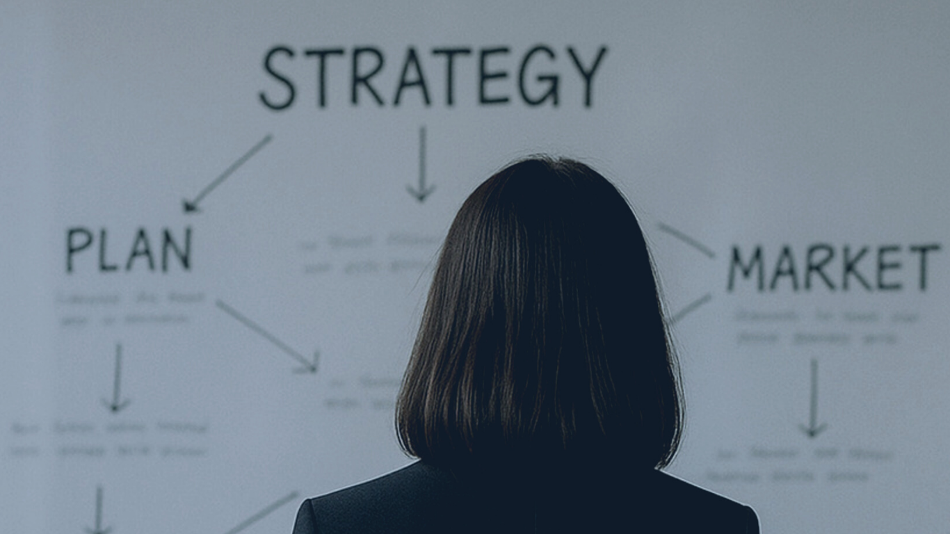 A woman is looking at a strategy diagram on a whiteboard that includes the words 'PLAN', 'MARKET', and the word 'STRATEGY' at the top with arrows connecting the concepts.