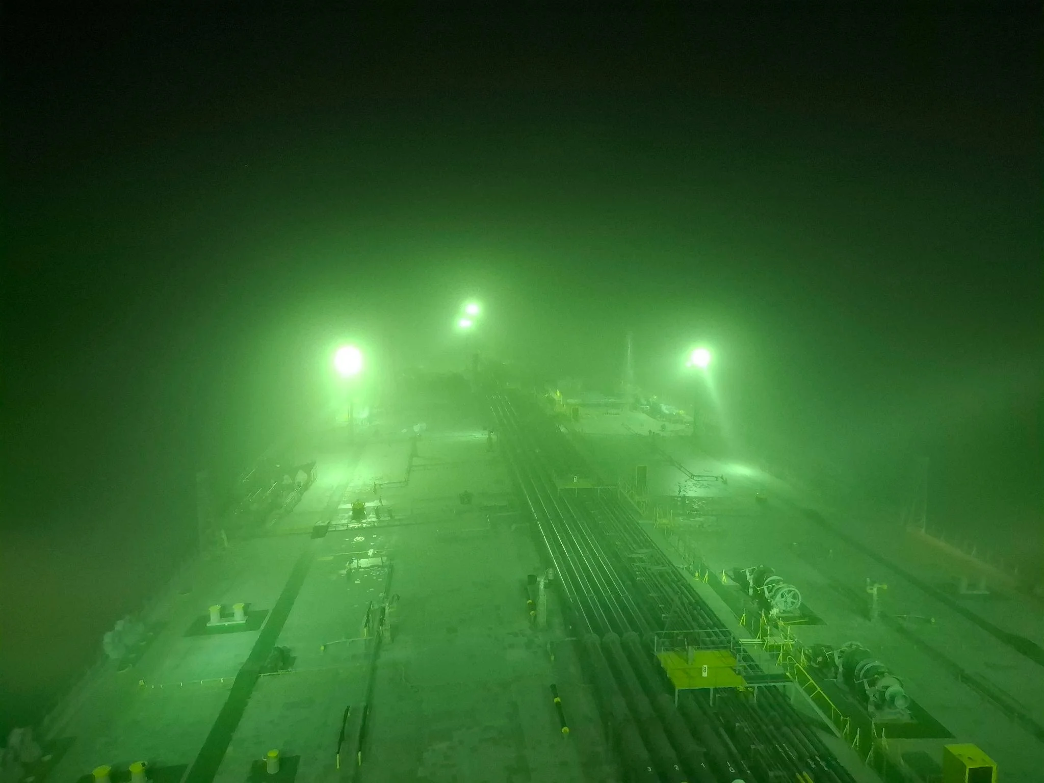 Green fog or laser lights at a construction or industrial site with visible pipes and equipment.