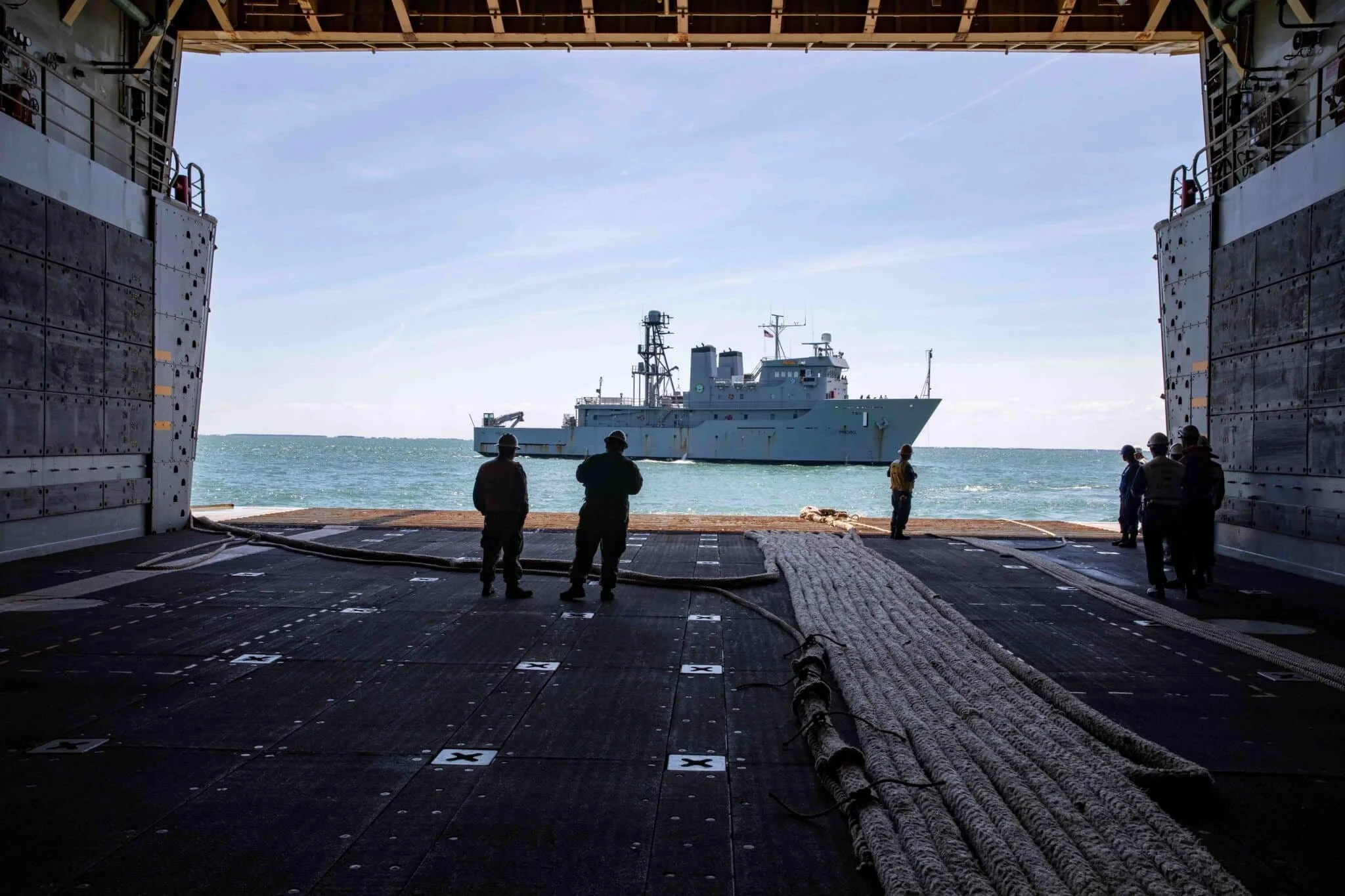 View from inside a ship opening, looking out at a military vessel on the water with seven sailors or soldiers standing on the deck.