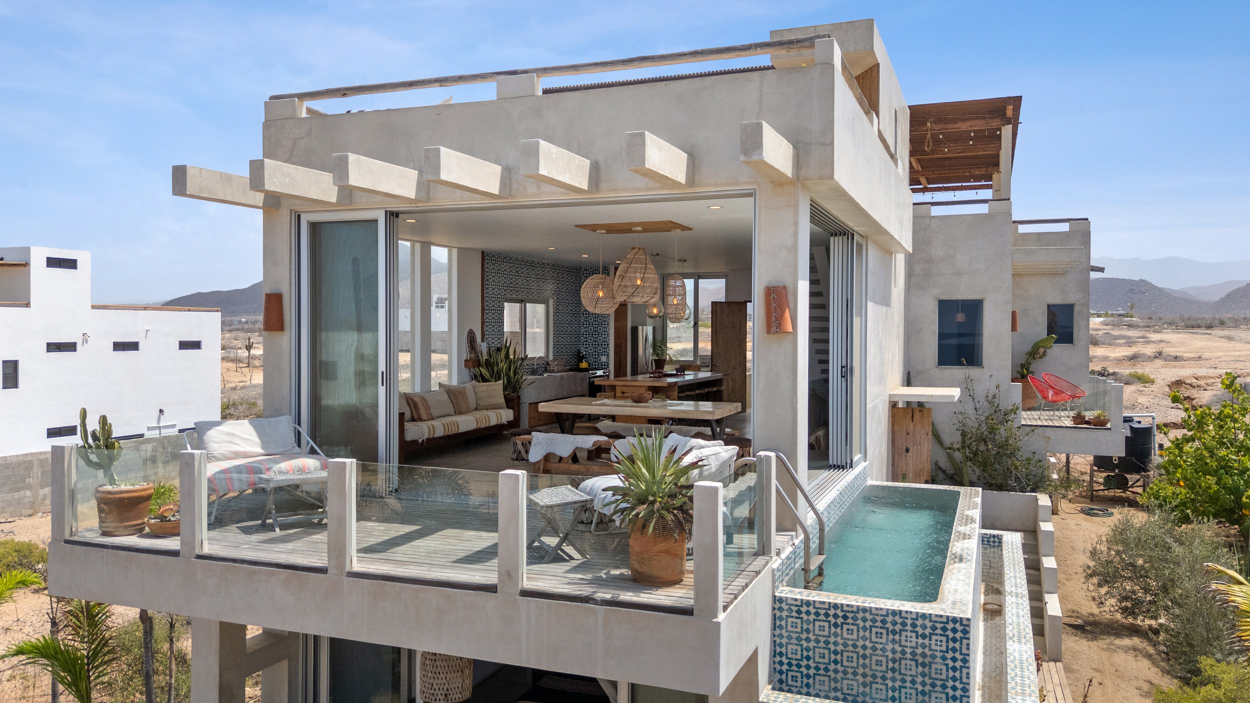 Modern house with an open living space, large glass doors, outdoor balcony with potted plants, and a small pool with tile accents.