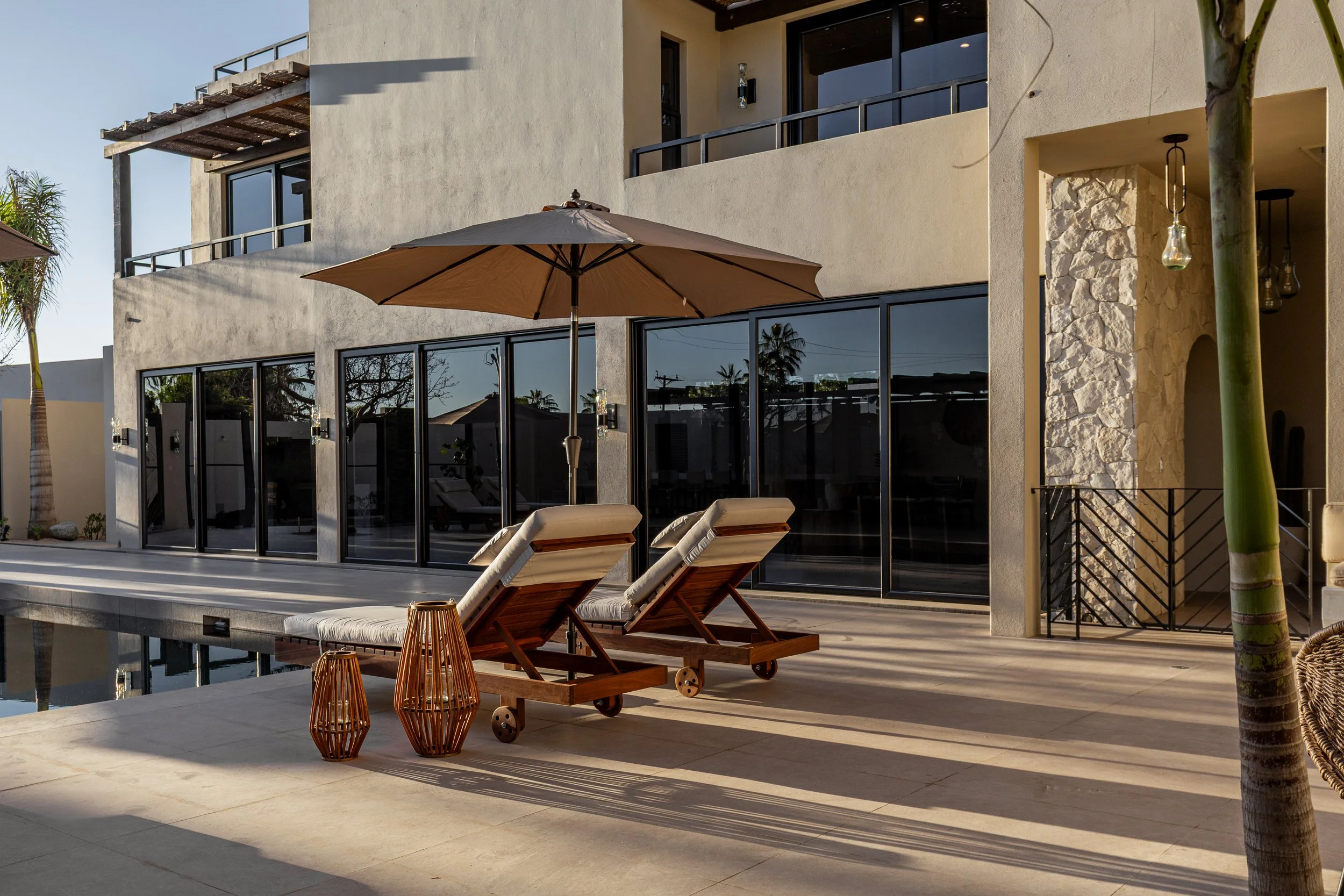 Modern house with large glass sliding doors, outdoor lounge chairs, umbrella, and decorative lanterns on patio
