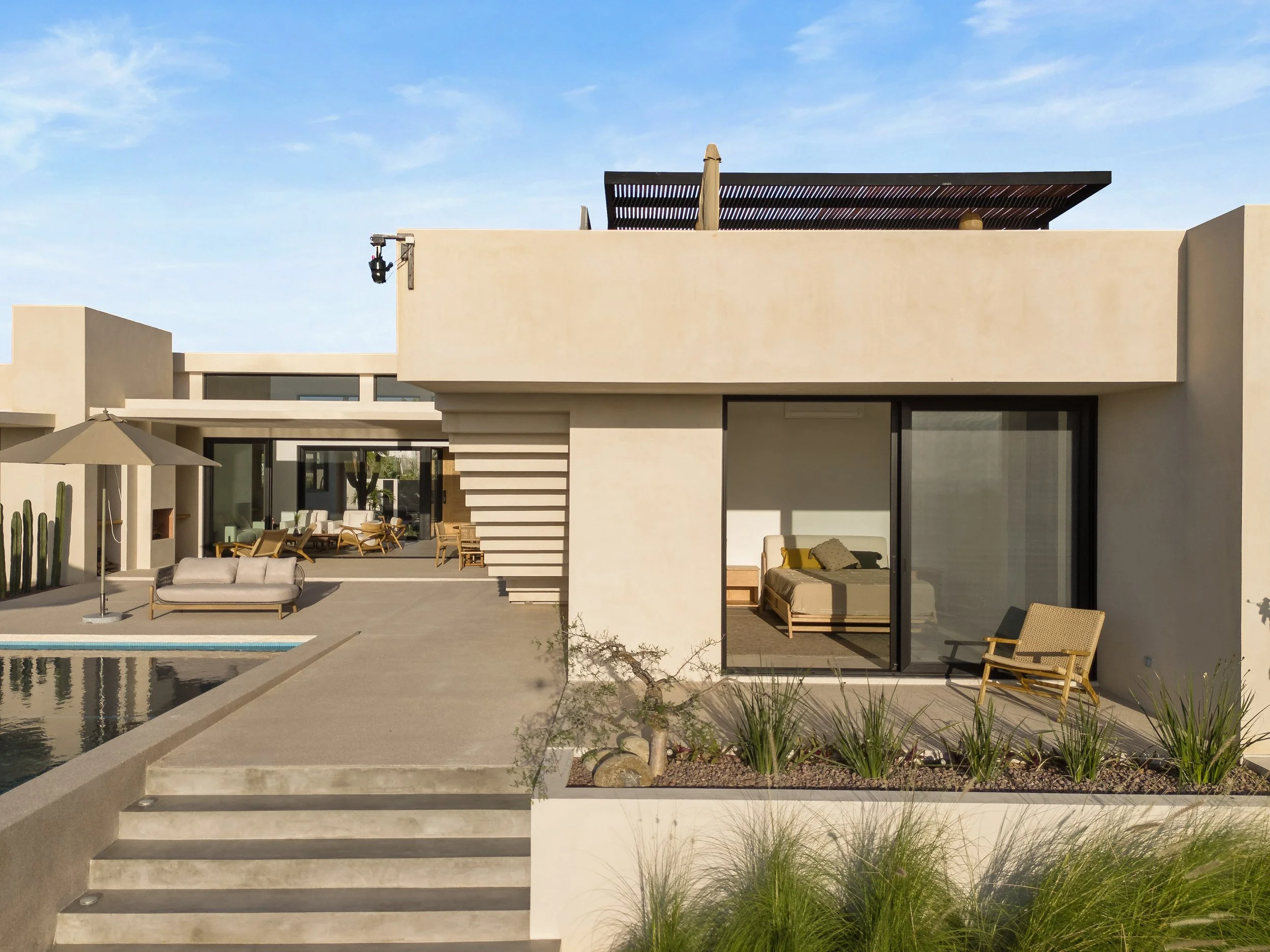 Modern house with outdoor seating area, pool, and desert landscaping, featuring large glass doors and minimalist design elements.