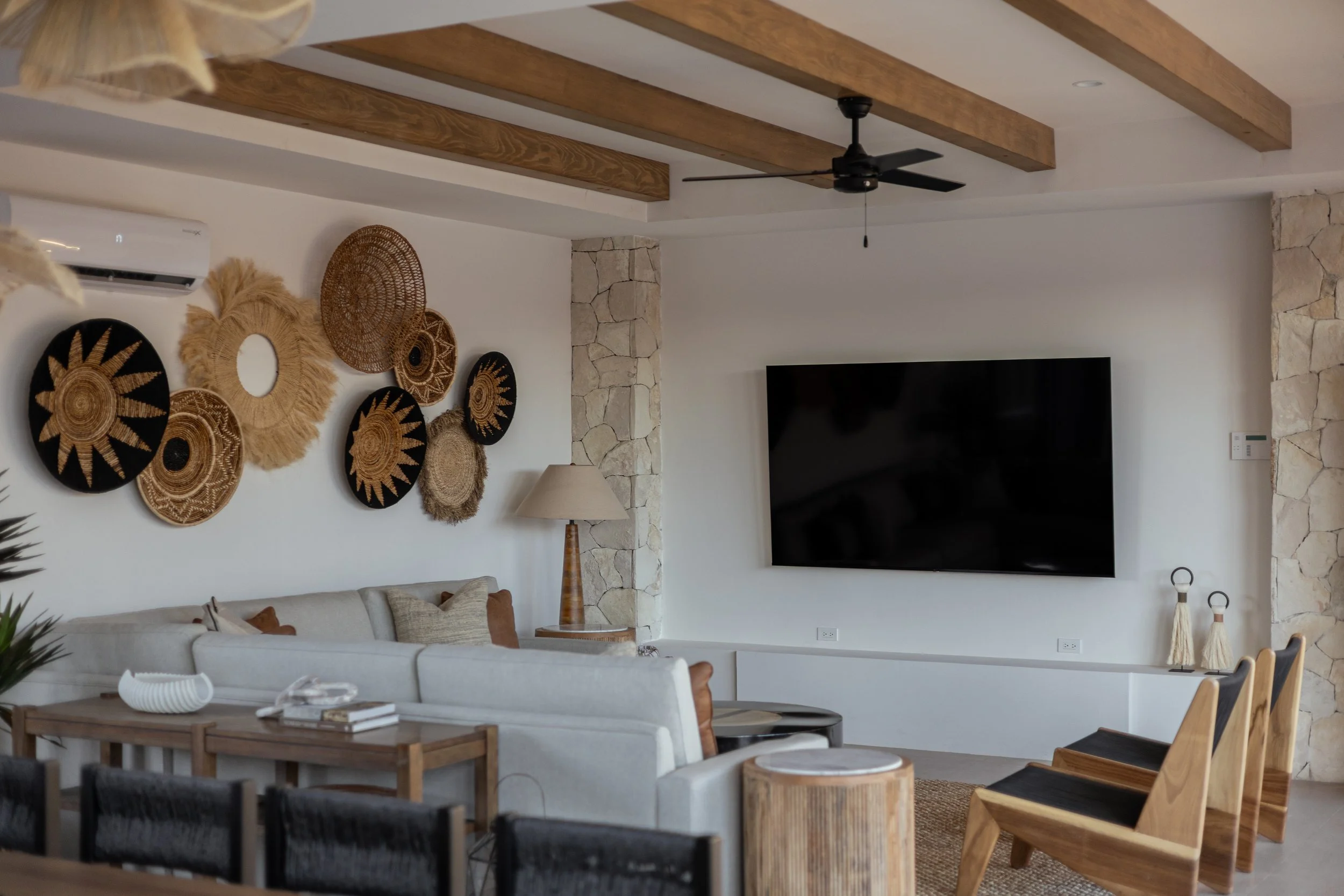 Modern living room with a white sofa, a flat-screen TV, and decorative woven wall hangings.