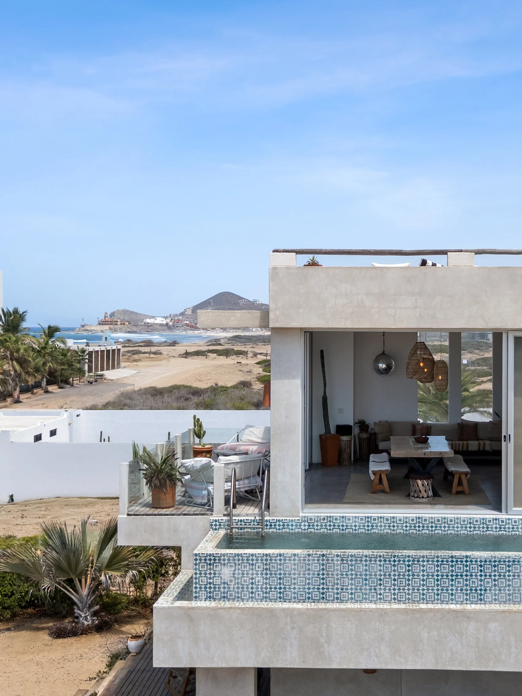 A modern coastal house with an outdoor patio, view of the beach and ocean, and a pool with intricate tiling.