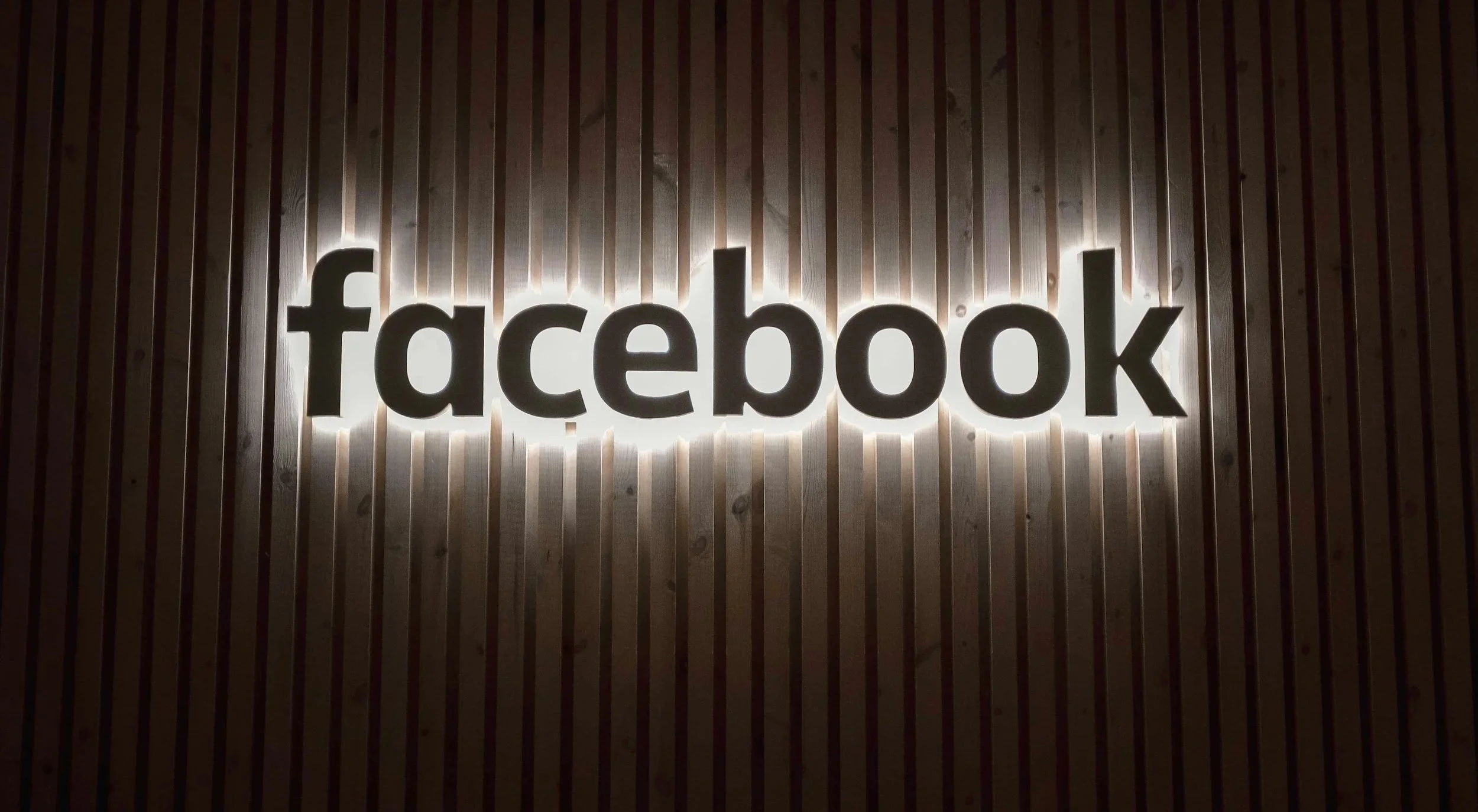 Backlit Facebook logo on a wooden wall.