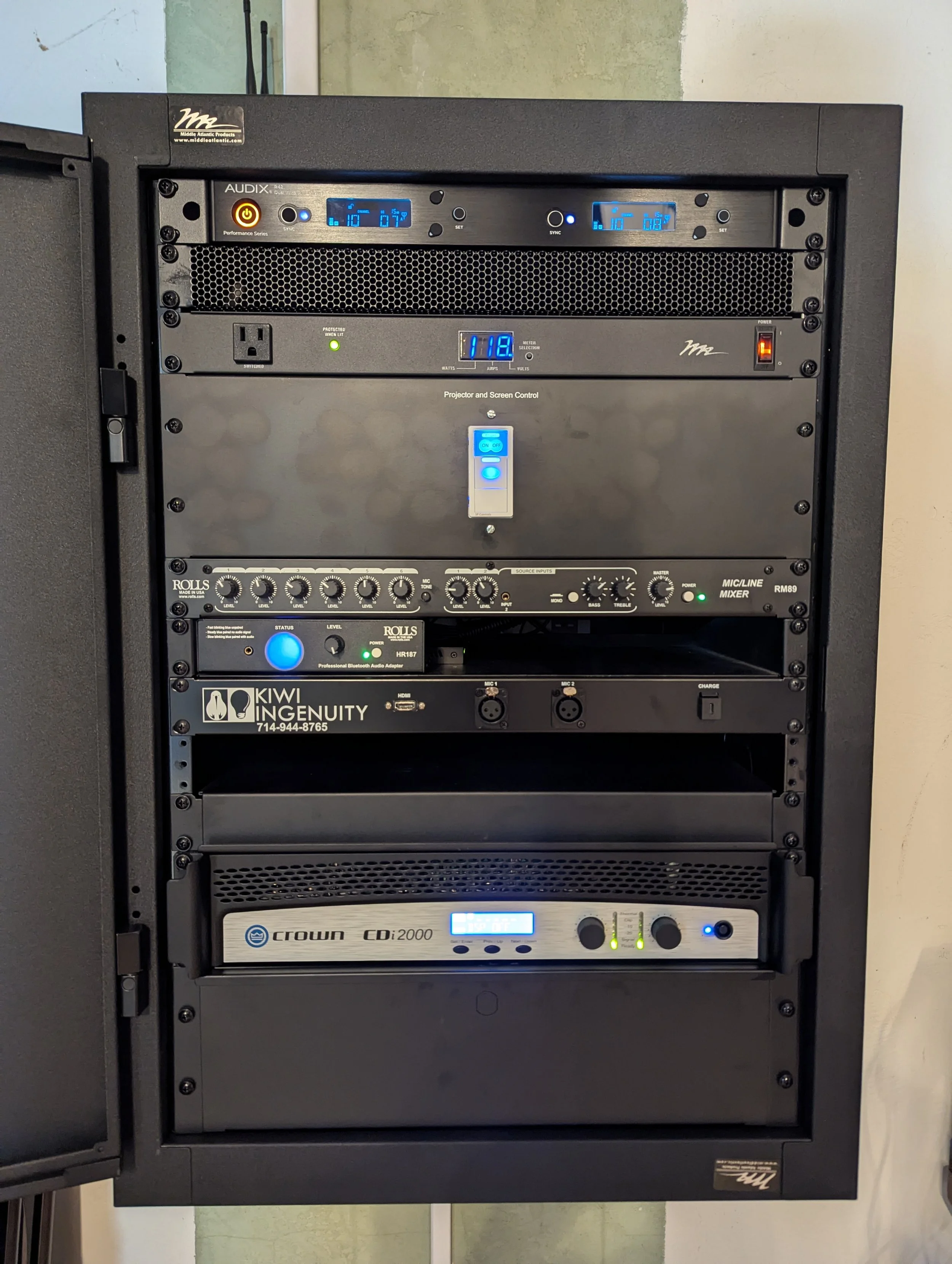 A sound equipment rack containing various audio and projection control devices, including amplifiers, mixers, and power supplies, with digital displays and controls.