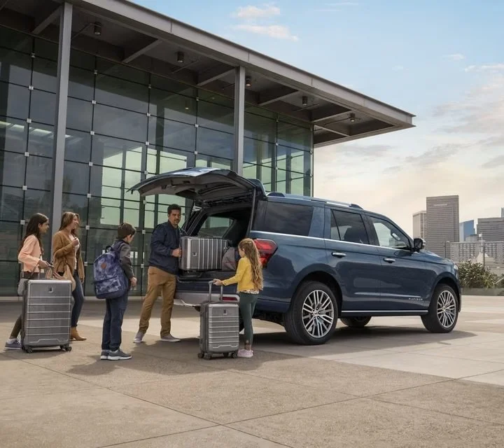 People loading luggage into the back of an SUV outside a modern building with glass walls, in an urban area with city skyline in the background.