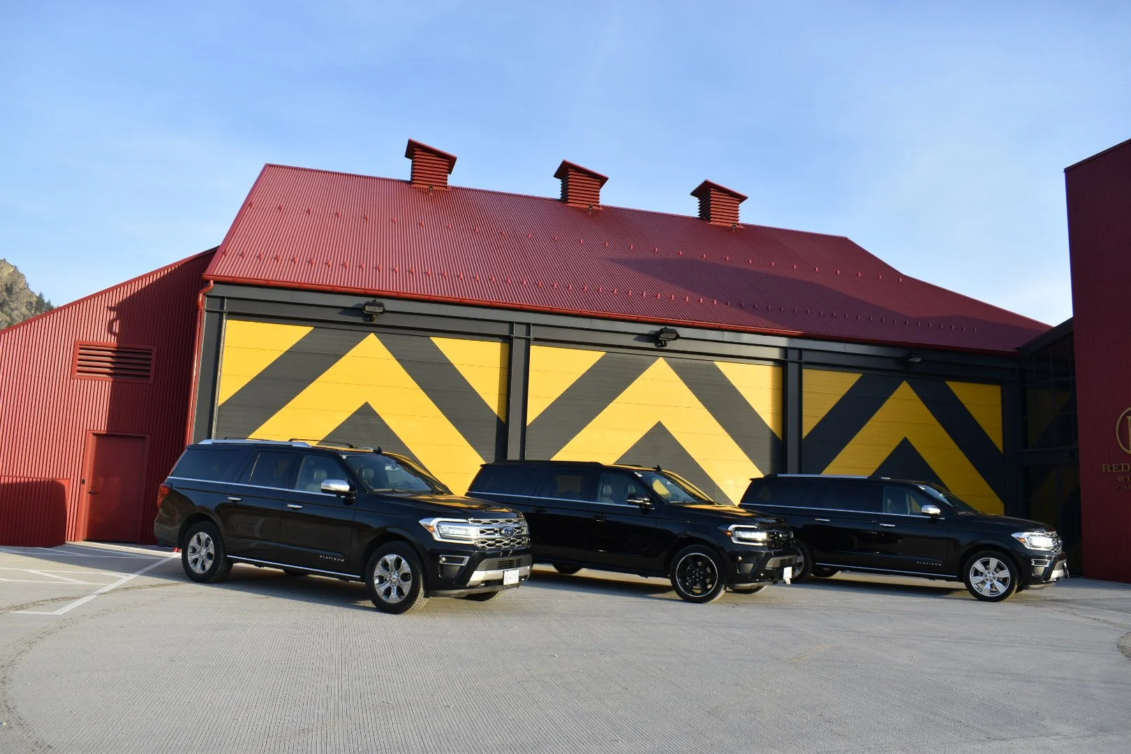 Three black SUVs parked in front of a red building with yellow and black geometric patterns on the garage doors.