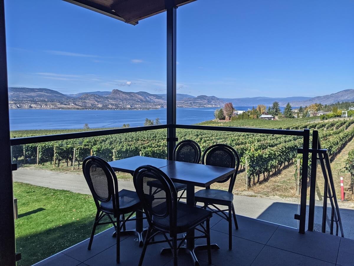 Patio with four chairs and table overlooking a vineyard, lake, and mountains under a clear blue sky.