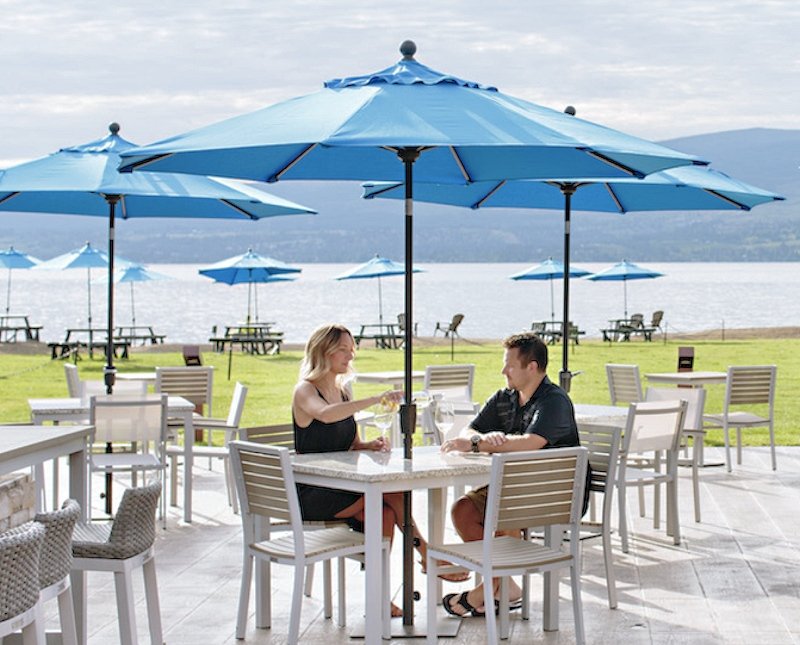 A couple dining outdoors under blue umbrellas by a lake