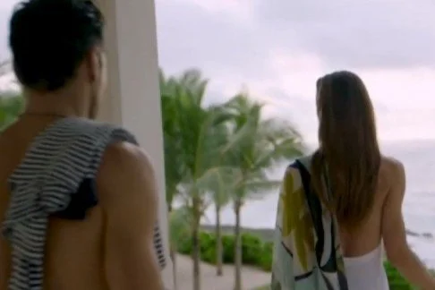 Two women on a balcony overlooking a beach with palm trees, facing away from the camera, during daytime.