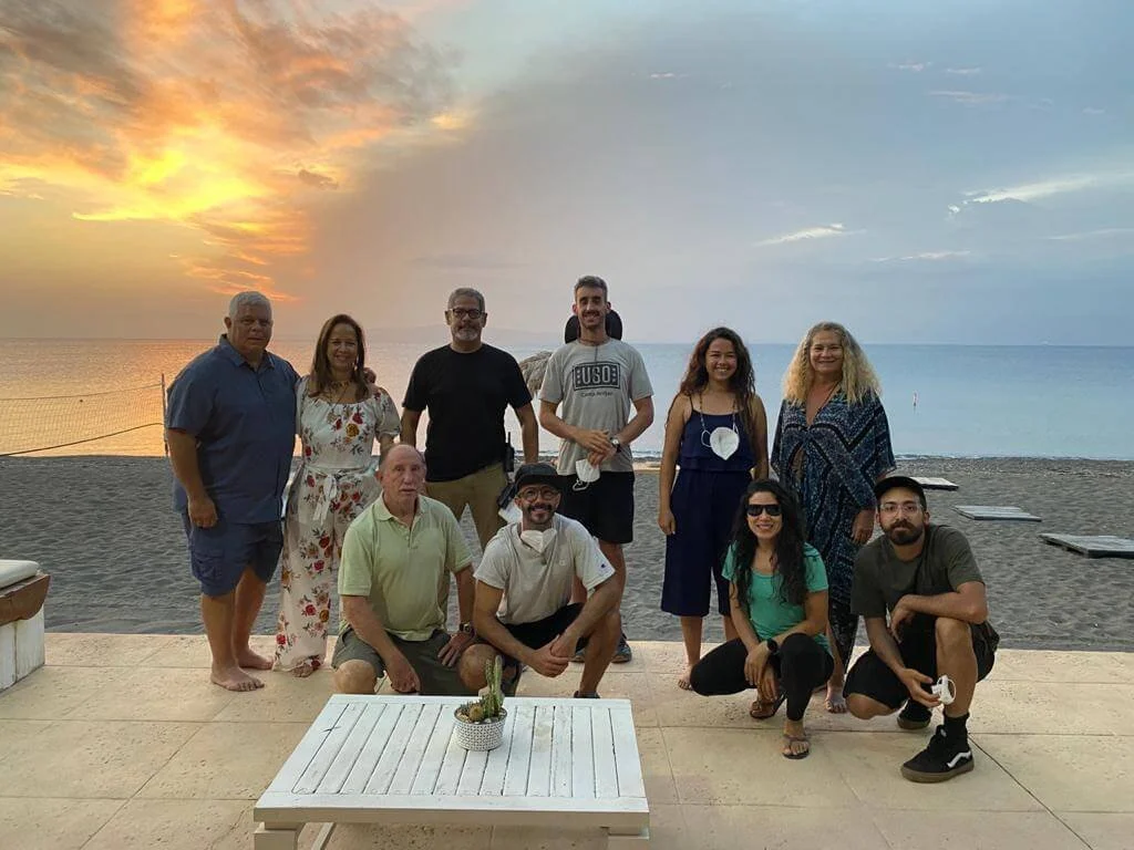 A group of eleven people posing on a beach during sunset with the ocean in the background.
