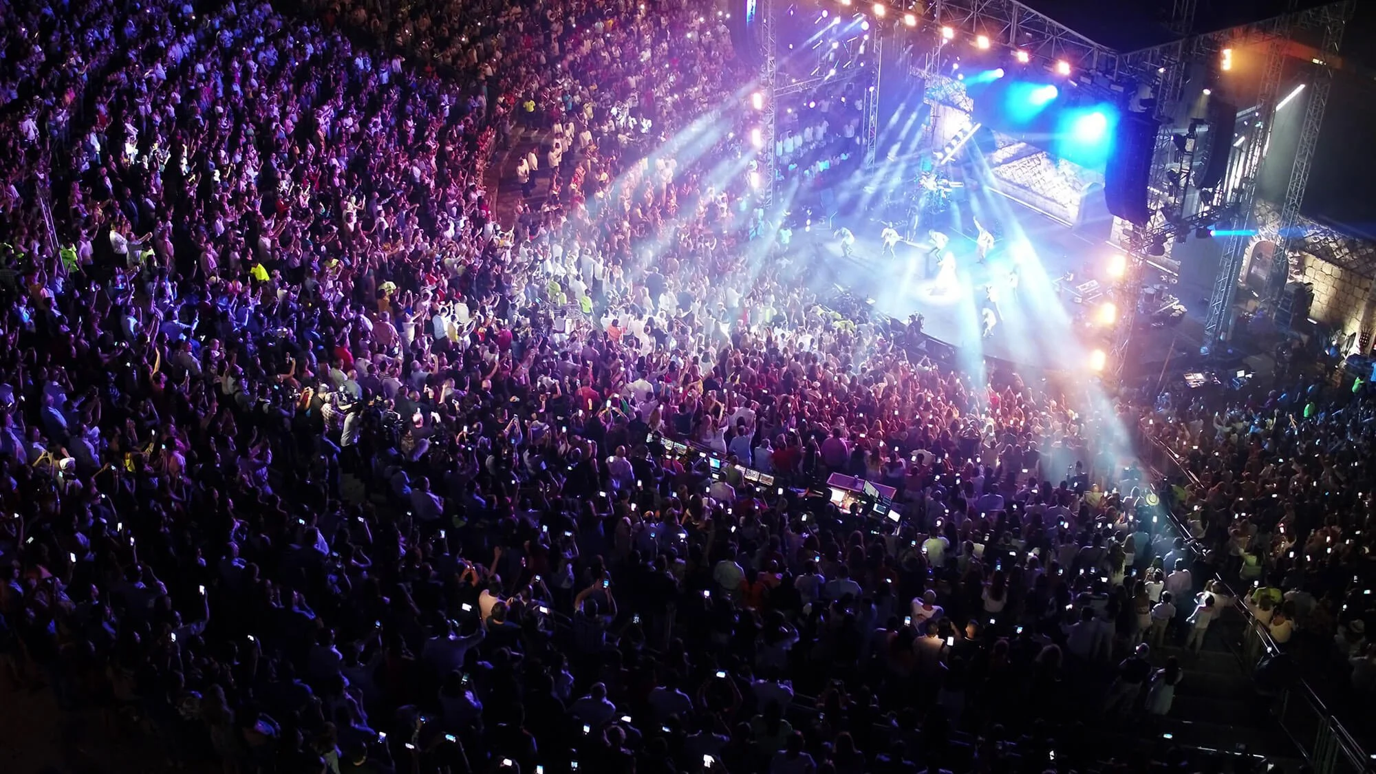 Crowd of people at concert with stage lights and performers.