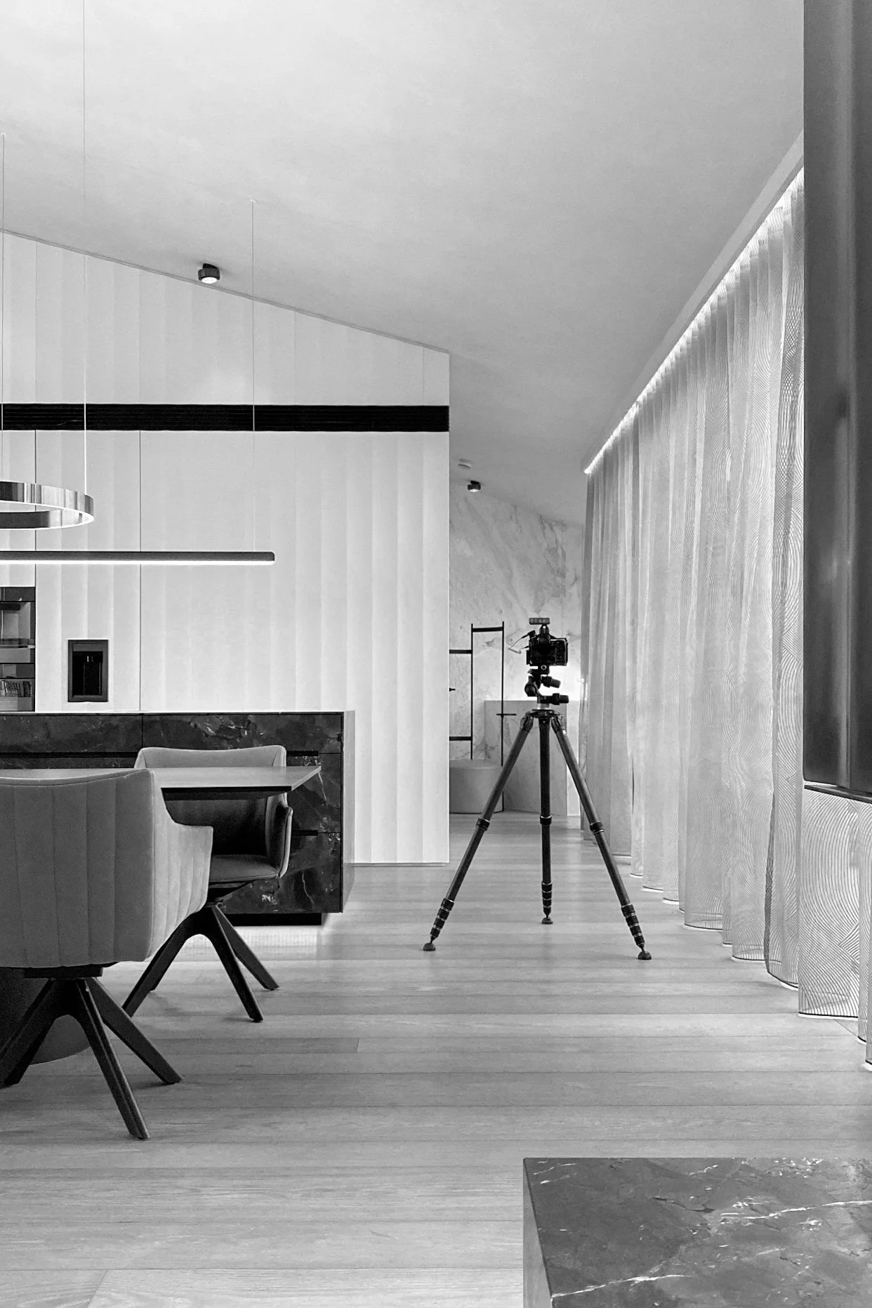 Modernes, minimalistisches Innendesign mit einem Dreibeinstativ und Kamera, große Fenster mit transparenten Vorhängen, Essbereich mit Tisch und Stühlen, helle Farbpalette, Holzfußboden.